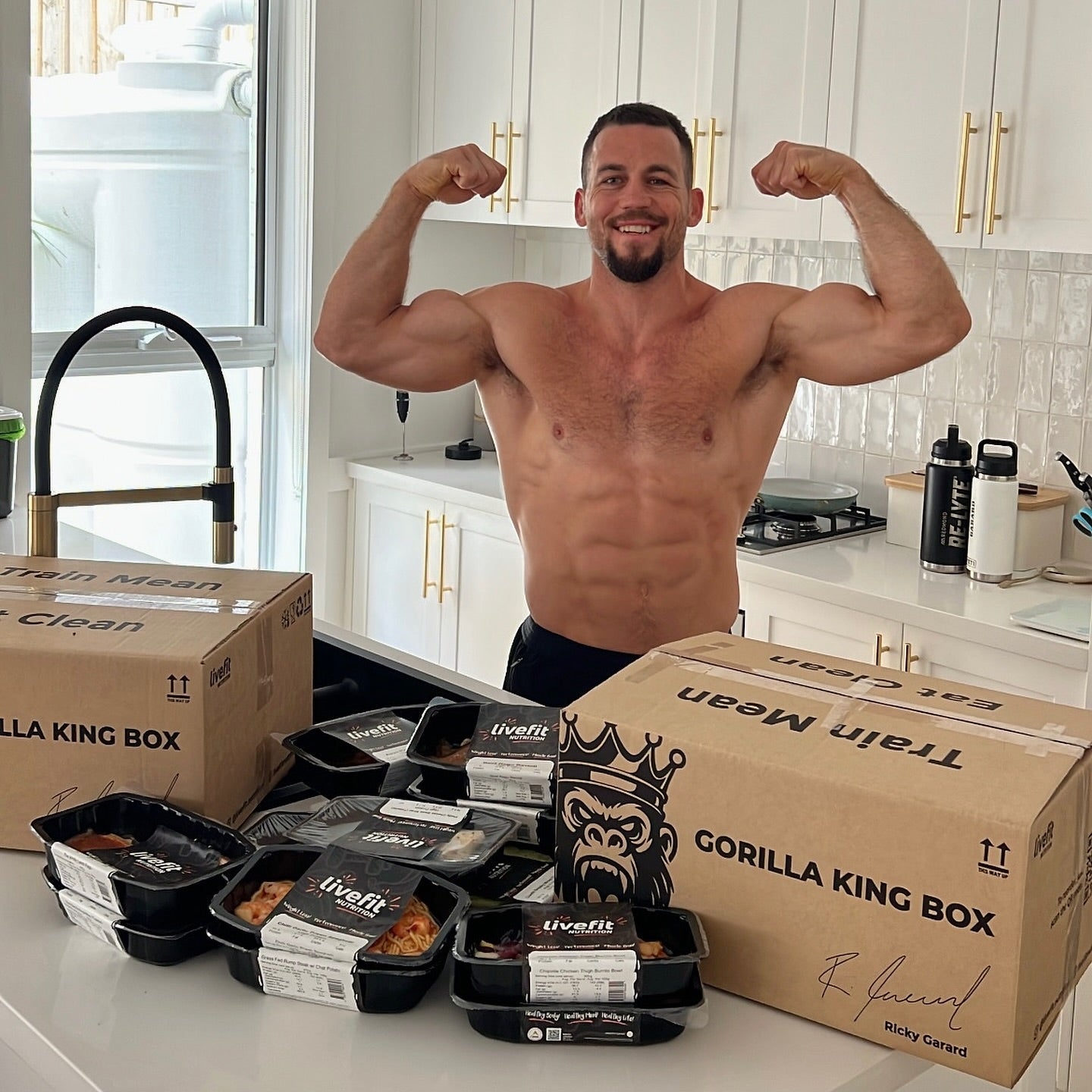 Man flexing muscles in a kitchen with 'Gorilla King' and 'Train Meal' boxes.